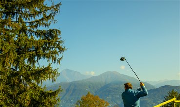 Golfer Teeing Off with His Driver with Mountain View in Autumn in Lombardy