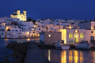 Traditional Greek whitewashed houses and church of Dormition of Mother of God on hilltop by seafront after sunset