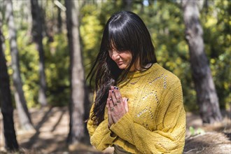 Woman meditates with hands clasped on the woods