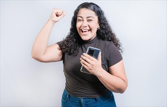 Winning happy young woman holding cell phone. Happy latin girl celebrating with phone isolated. Happy people holding smartphone and celebrating