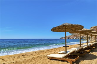 Beautiful empty beach with sun umbrellas and sunbeds. Perfect summer destination. Straw sunshades and sunbeds on the empty beach with blue sea and rocky hills. Vacations in Greece