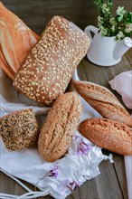 Different types of handmade rustic bread made of seeds on a pink cloth on a wooden table decorated with flowers