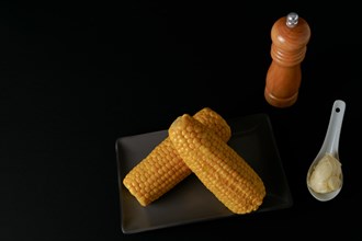 Corn cobs with pepper pot and spoon with butter