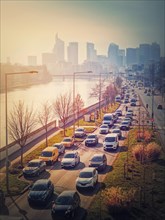 Busy traffic on highway and city streets creating high pollution and smog. Urban sunset view across Seine river to La Defense metropolitan district