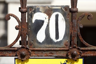 Old weathered house number sign number seventy and decorated metal garden fence