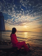 Woman relaxing on the sunbed as meets the dawn at the beach. Beautiful sea sunrise scene