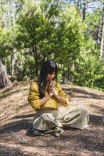 Woman with hands clasped meditating on the woods. Vertical Shot