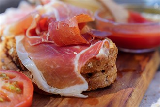 Close-up of a typical Spanish acorn-fed iberian ham and tomato toast on a wooden board with a bowl of freshly crushed tomatoes