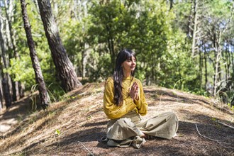 Woman with hands clasped meditating on the woods