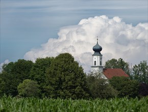 Bavarian Onion Church behind field and trees in front of big white cloud