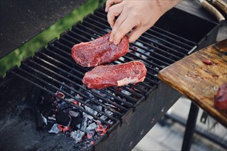 Unrecognizable man put raw strip steaks on hot grid of grill