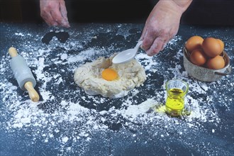 Woman adding eggs to a dough of flour to make bread on a black wooden table with olive oil