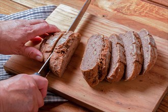 Woman cutting slices of rustic bread with a knife on a wooden board