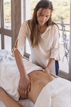 Young woman therapist performing relaxing and shaping massage on patient's belly