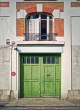Town building facade with a green garage gate and window with louvers above the door