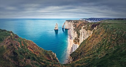 Falaise d'Aval limestone cliffs washed by La Manche channel waters. Beautiful coastline panorama with view to the famous rock Aiguille of Etretat in Normandy