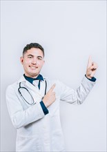 Handsome doctor pointing a promotion with finger isolated. Happy latin doctor pointing at advertising space isolated