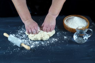 Woman kneading with her hands a flour dough to make homemade bread on a black wooden table with flour