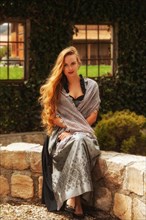Woman with long hair and festive dirndl sits on a stone wall