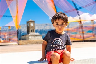 Portrait of a child in the colorful arches in the Ottoman Castle Fortress of Gjirokaster or Gjirokastra and in the background the church with the clock tower. Albania