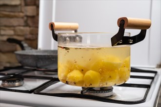 Boiling potato with seasoning in transparent glass pot on a gas stove