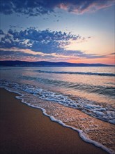 Sunrise at the sea with foamy waves on the sand and colorful sky at the horizon. Summer and travel background