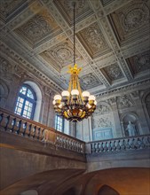 Architectural details of a ornate staircase hall with a glowing vintage chandelier hanging from ceiling at Versailles Palace