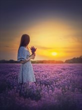 Side portrait of a young woman in dress stands in the purple lavender field looking at the beautiful sunset sky. Natural summer dusk scene