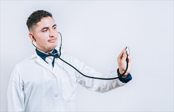Male doctor holding stethoscope on white background. Portrait of latin doctor holding stethoscope with copy space