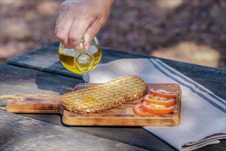 Woman pours virgin olive oil on a toast of bread with fresh tomatoes on a wooden table