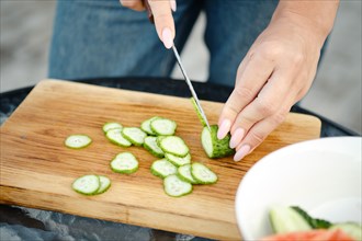Unrecognizable woman slicing fresh cucumber for salad