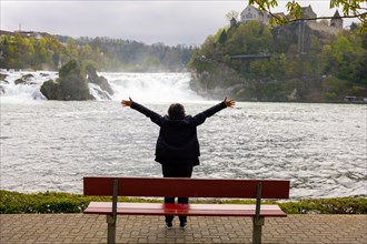 Woman with Arms Outstretched on a Bench in Front of Rhine Falls at Neuhausen in Schaffhausen