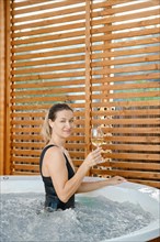 Happy woman standing in profile with a glass of wine in outdoor hot tub