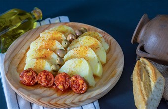 Boiled potato with paprika and fried chorizo on a wooden board with a bottle of extra virgin olive oil flavored with rosemary