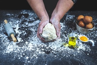Woman with bread dough in her hands on a black table with flour