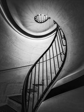 Black and white abstract view of a stairwell with metal handrail. Spiral stairway
