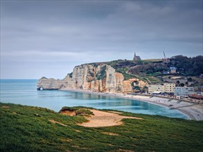 Sightseeing view to Etretat coastline with the famous Notre-Dame de la Garde chapel on the Amont cliff. Seashore washed by Atlantic ocean waters