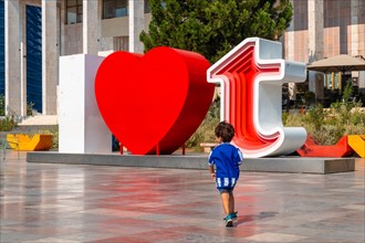 A child in the I Love Tirana sculpture at Skanderbeg Square in Tirana reflected. Albania