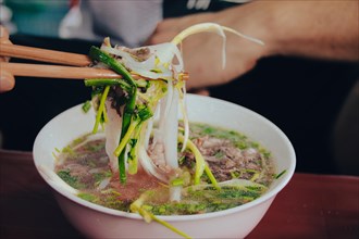 Eating a bowl of authentic traditional Vietnamese beef noodle soup called pho bo