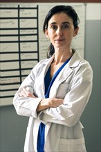 Positive brunette healthcare worker woman in white uniform looking at camera and crossing her arms