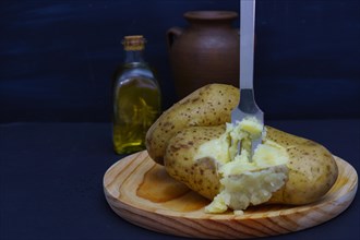 Boiled potato opened with a fork on a wooden plate