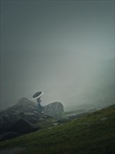 Man with umbrella climbing a mountain hill in a gloomy weather with dense mist. Moody hiking scene with a wanderer walking on the cliffs of the foggy valley