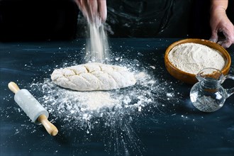 Woman pouring flour on a fresh dough to make homemade bread on a wooden table with flour