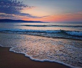 Dawn at the sea with foamy waves on the sand and colorful sky at the horizon. Sunny Beach coastline in Bulgaria. Summer and travel background
