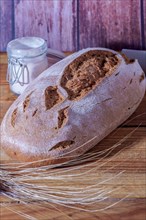 Loaf of rustic rye bread on a wooden table with flour and rye dowels