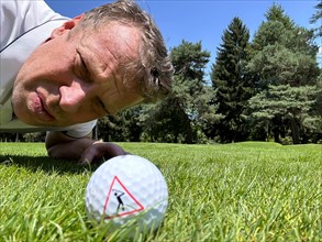 Golfer Looking at a Golf Ball with Warning Sign on the Fairway in a Sunny Day in Switzerland