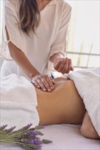 Woman masseuse with patient on massage table placing oil on her abdomen