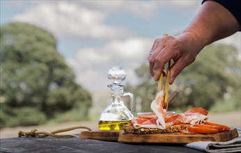 Woman putting slices of acorn-fed iberian ham on a slice of bread with tomato and olive oil on a wooden table in the countryside