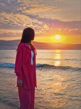Aesthetic young woman portrait wearing pink suit on the sea shore as meets the dawn. Beautiful sunrise at the beach. Summer vacation background