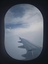 Plane flight through the dense foggy clouds. Airplane wing seen through the window